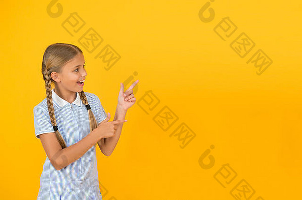 看看这个。快乐的小女孩指着黄色背景的复印空间。回到学校。注意概念。广告模式。女学生展示学校产品。积极的孩子。