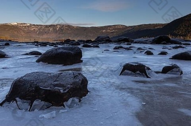 挪威峡湾潮汐下降时，<strong>黑色岩石</strong>巨石穿过薄冰架。