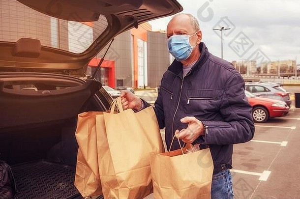 一名脸上戴着防护面具的男子将食品包装装入汽车。食物递送。冠状病毒CVID-19
