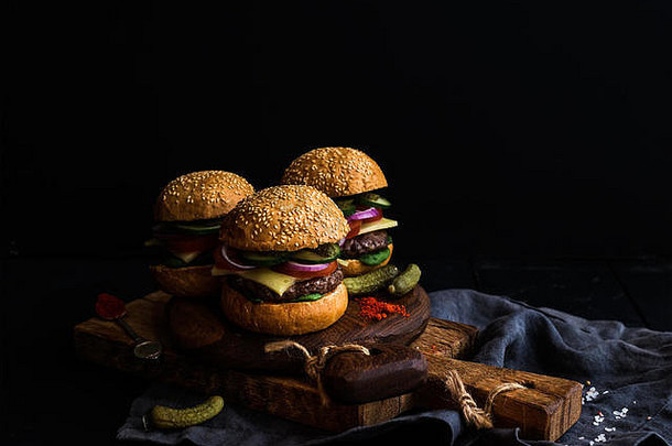 新鲜<strong>牛</strong>肉汉堡配腌菜和调味品，在质朴的木板上，黑色背景。