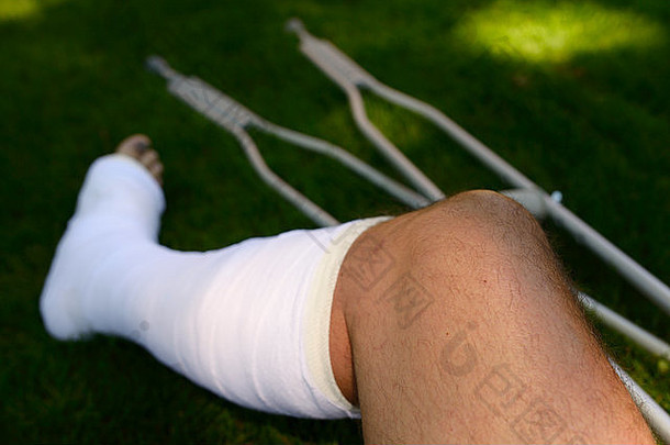 一个受伤的男子，腿在石膏中，拄着拐杖在草坪上