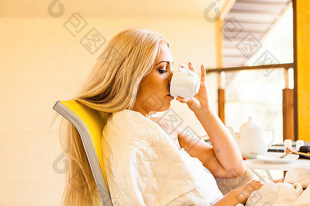 可爱的年轻的女人喝早....咖啡坐着椅子窗口早....醒着的概念