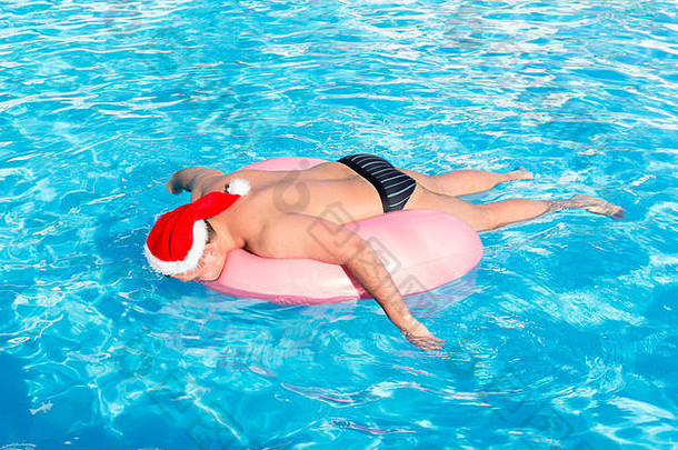 一个戴着圣诞老人帽子的醉汉在游泳池里的充气圈上游泳。俄罗斯游客的旅行。