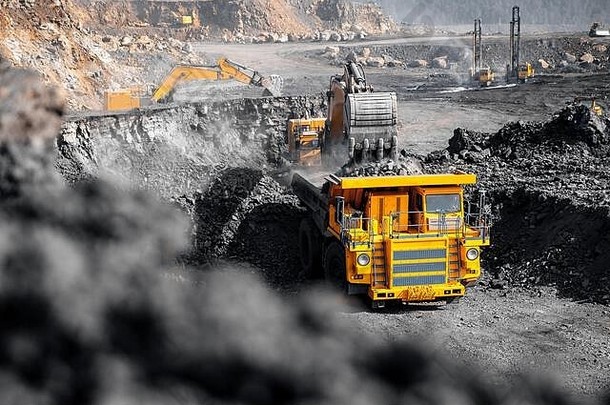 露天矿工业。挖掘机将煤炭装载到黄色矿用卡车中