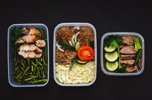 黑色背景容器中的健康食品：零食、晚餐、午餐。烤鱼、豆类、牛肉片、土豆泥、肉类和蔬菜