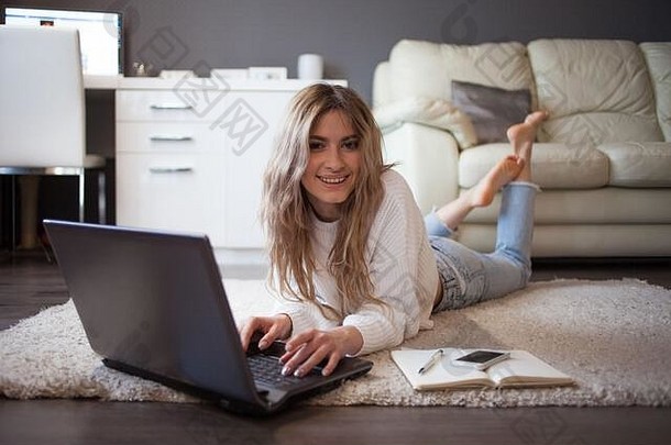 远程沟通在线工作可爱的年轻的女人说谎地板上软地毯移动PC