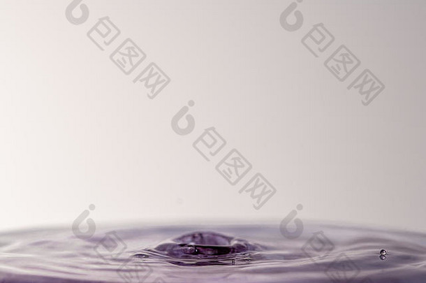 一个紫色水滴在浅色白灰色背景下溅入水中的特写微距摄影