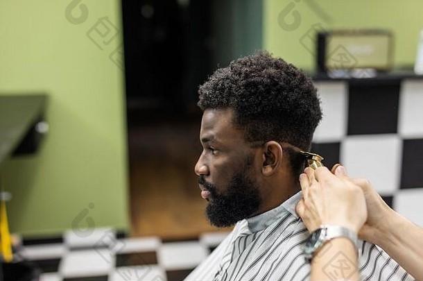 专业理发师用电动剃须机做新发型。年轻的黑人男子在理发店理了一个新发型。