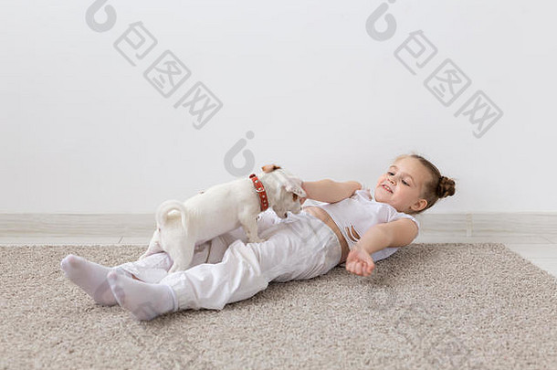 宠物的主人，孩子和狗的概念-小女孩和可爱的小狗躺在地板上玩耍