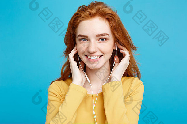 生活方式理念——欢<strong>快快</strong>乐的姜红色头发女孩的肖像，戴着耳机欣赏音乐，对着镜头欢快地微笑。在蓝色粉彩背景上隔离。空间。