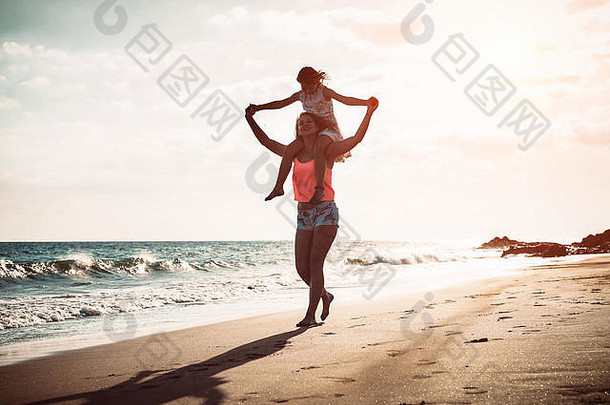 妈妈。女儿运行海滨海滩快乐家庭肩扛日落