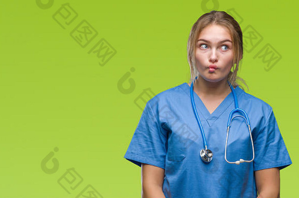 年轻的白人女医生穿着外科医生制服，在孤立的背景下做着鱼脸和嘴唇，疯狂而滑稽的手势。滑稽的表情。
