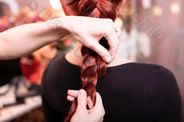 美丽的红发长发女孩，在一家美容院，理发师编织了一条法国辫子。专业的护发和发型设计。