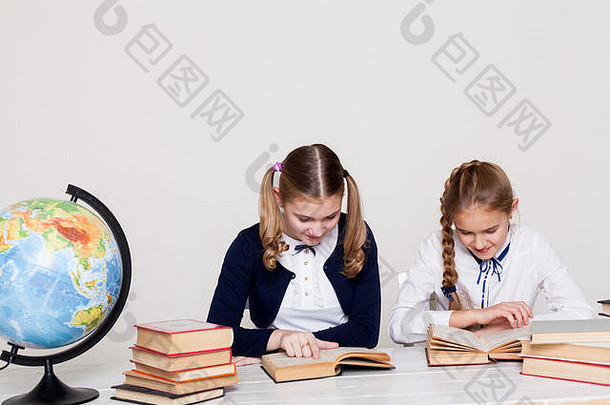 两个女学生坐在课桌旁，手里拿着书和笔记本