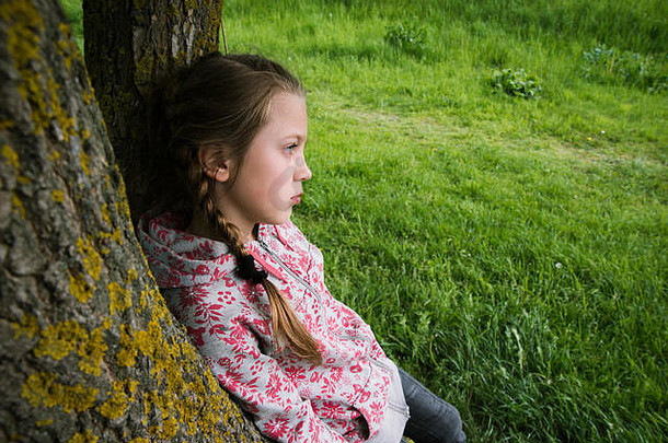 小女孩倚着树干在户外沉思