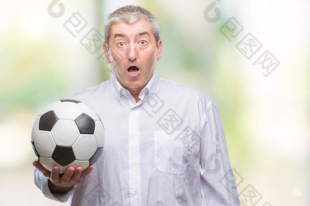 英俊的老年男子在孤立的背景上拿着足球，吓得面目全非，恐惧的表情使他既害怕又兴奋