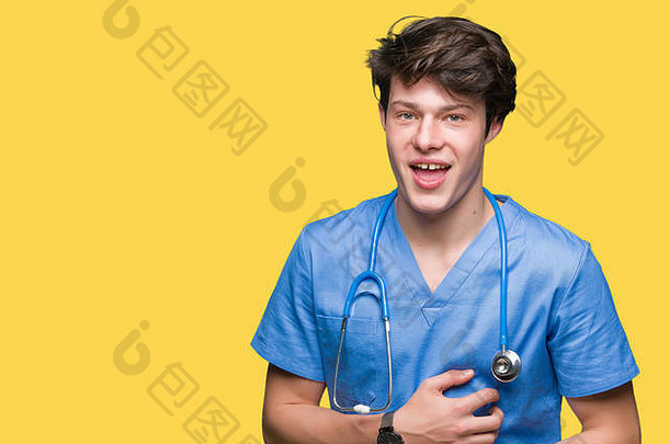 年轻的医生穿着医疗制服，在孤立的背景下微笑着，大声大笑，因为这是一个有趣的疯狂笑话。高兴的表情。