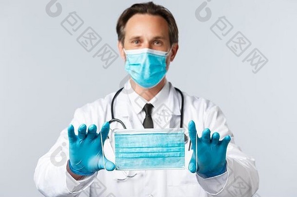 2019冠状病毒疾病、医务人员和疫苗接种的概念。戴PPE的中年医生，推荐医用口罩品牌，讲解如何戴口罩预防
