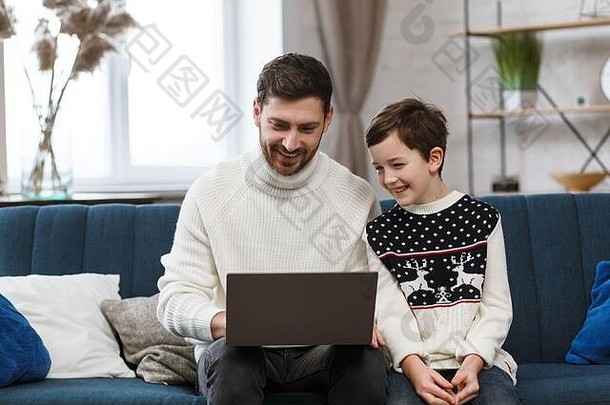 呆在家里。微笑的父子使用笔记本电脑进行在线会议、视频通话、与亲戚的视频会议、家庭教育的肖像。快乐的