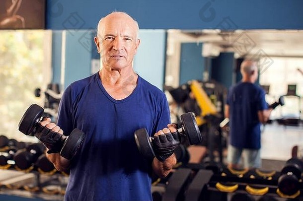 一个秃顶的老人在健身房练习哑铃的肖像。人、健康和生活方式概念