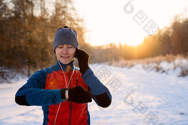 穿着保暖运动服戴着耳机的跑步者看着一个现代智能时钟