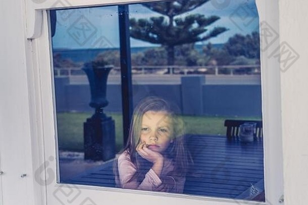 2019冠状病毒疾病隔离期间，沮丧而孤独的小女孩透过窗户看。当科罗纳病毒流行时，孩子们感到悲伤