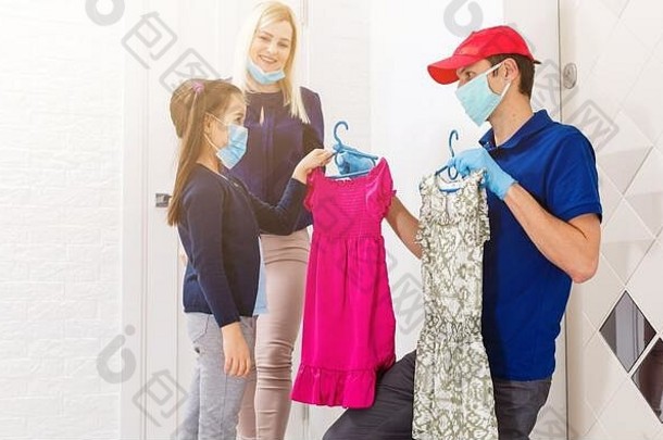年轻的女人女儿穿医疗面具接收orderd食物交付男人。在室内预防病毒传播