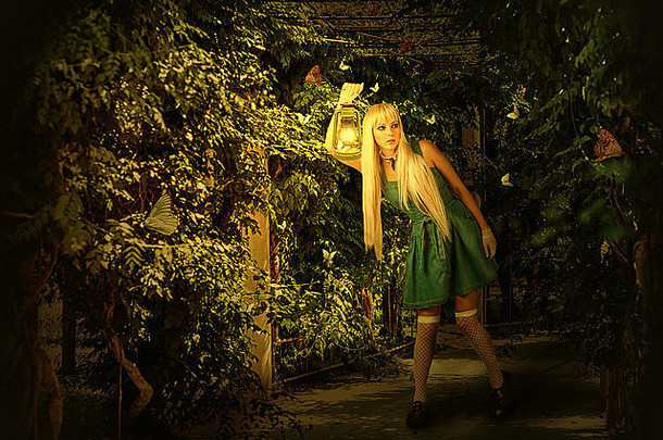 年轻的金发女郎穿着衣服，走在一条神秘的小路上，走进一片迷人的森林。她拿着煤油灯