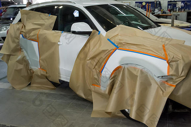 在车间为白色汽车喷漆以进行车身维修。SUV车上覆盖着纸，以免撞到油漆。