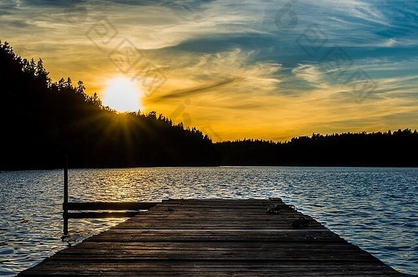 日落时，一个木制码头伸入瑞典湖水中的对称广角视图，远处有松树