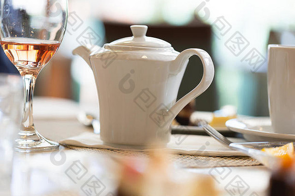 豪华餐厅桌子上的茶壶，紧挨着装有玫瑰红葡萄酒的玻璃杯。低角度透视聚焦在茶壶上