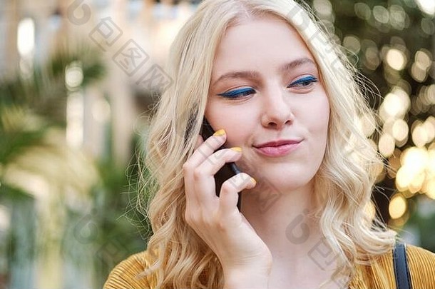 在户外打手机时，美丽的金发碧眼女孩狡猾地看着别处