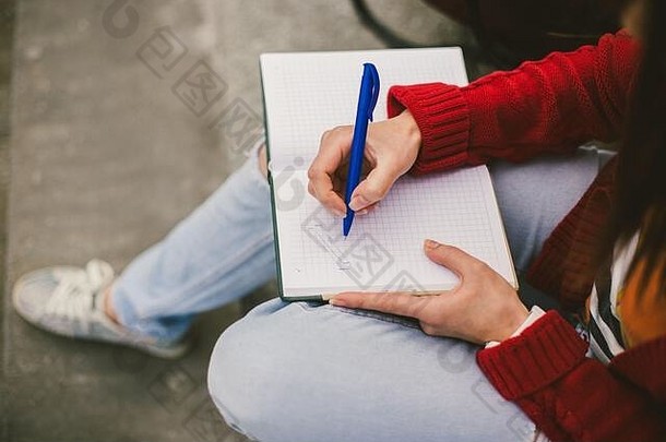 美丽的女孩坐在街上，手里拿着笔记本和钢笔，做笔记，休息。