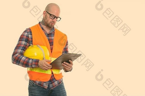 秃肌肉发达的男人。建设工人持有安全头盔阅读剪贴板