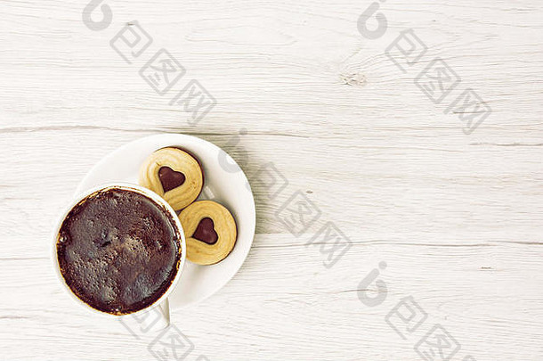 一杯黑咖啡，木质背景上有两块心形果酱饼干。将文本放置在右侧。饮食