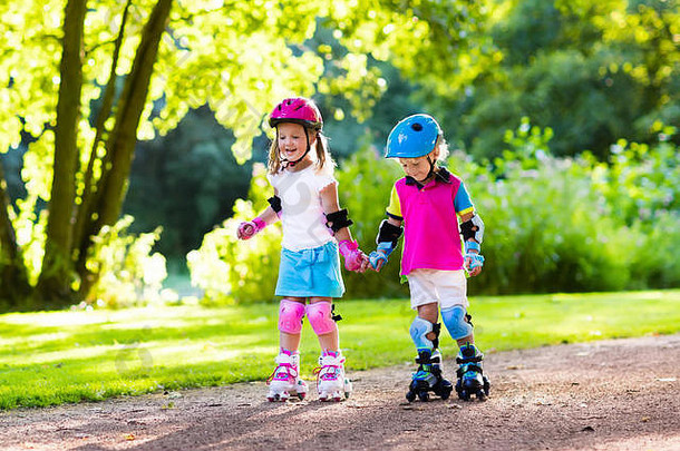 女孩男孩学习辊滑冰夏天公园孩子们穿保护垫安全头盔安全辊滑冰骑活跃的户外热点;