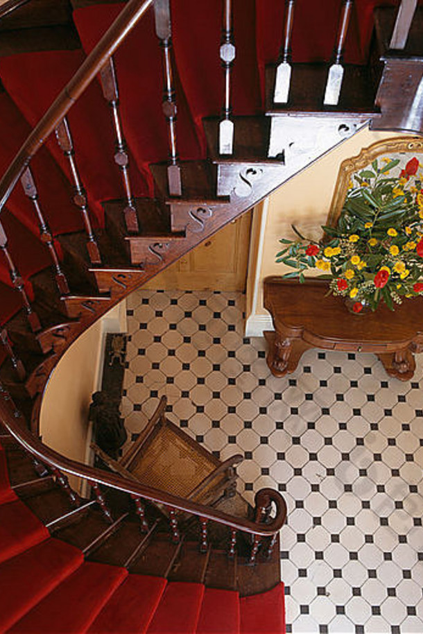 鸟瞰传统大厅中红木弯曲楼梯和红地毯，黑色 白色棋盘格瓷砖地板