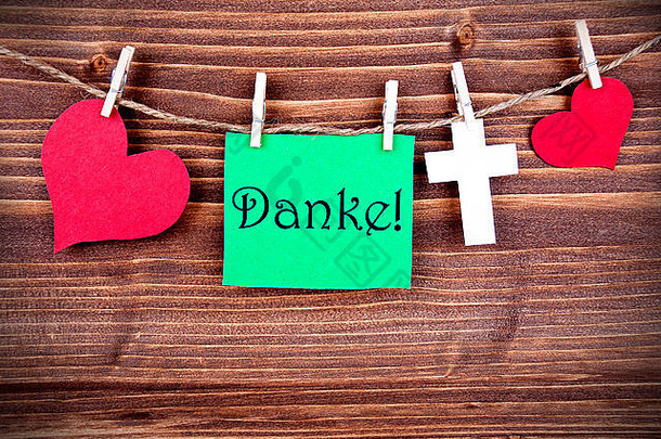 绿色标签或带有心形和十字的标签，在一行上有德语单词Danke，意思是木制背景上的感谢，三个Sy