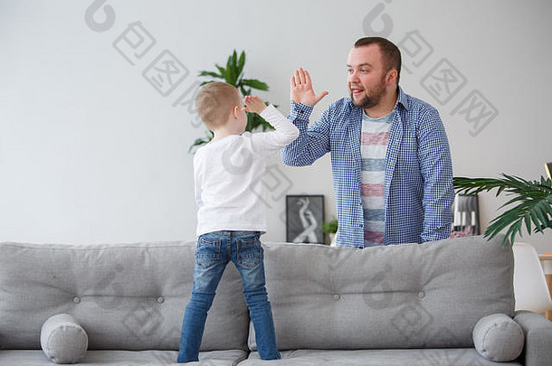 小儿子站在沙发上与父亲握手的家庭形象