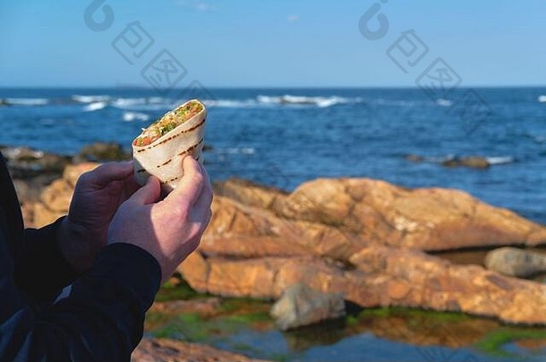 人们正在孤零零的岩石海岸吃外卖食物。食品配送和外卖、可回收容器、孤独午餐概念