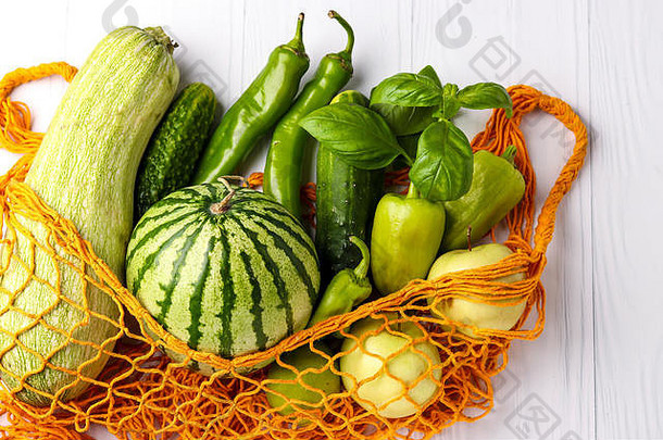白色背景下橙色可重复使用购物网袋中的绿色蔬菜和水果：西葫芦、黄瓜、甜椒、辣椒、苹果、梨、水