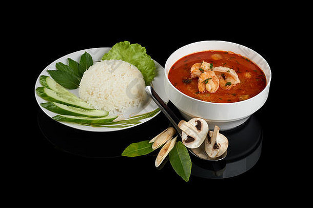 Tom yum或Tom yam是一种酸辣泰国汤，通常与虾一起烹调。配米饭、蔬菜和筷子。在黑稀土上分离
