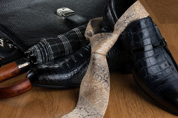 木制拼花地板上的经典蓝色鞋子、领带、雨伞和黑色公文包。特写。时尚和商业背景。