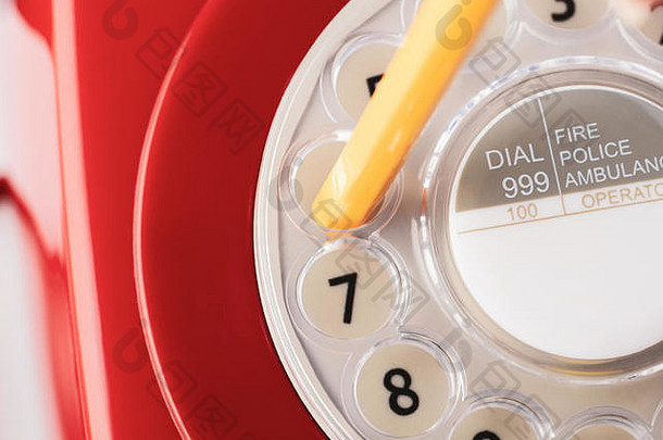 20世纪60年代至70年代复古红色电话机的特写镜头，黄色铅笔准备拨号。