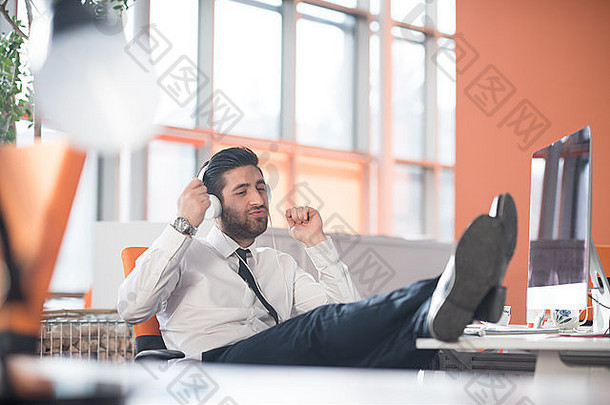 在现代创业公司办公室，留着胡子的快乐的阿拉伯年轻商人戴着耳机听<strong>音乐</strong>