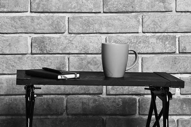 黄色茶杯或咖啡杯或陶瓷杯，用于饮用。在砖纹理背景上，本和黑笔托盘