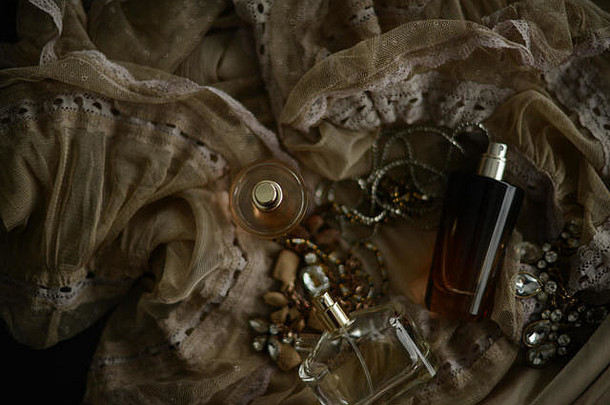 三个香水瓶和一条项链，背景为米色丝绸和蕾丝