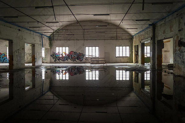 一个废弃工厂的内部，一个带有大窗户的棚子的图像反射在一个水坑的水中，urbex