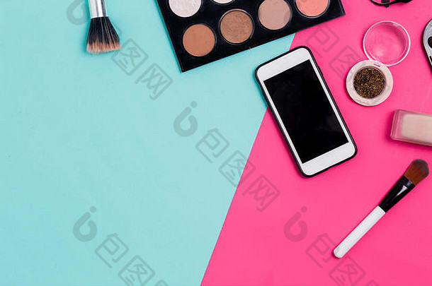 彩妆产品和智能手机的平面布置在彩色蓝色和粉色背景上，并留有复印空间。