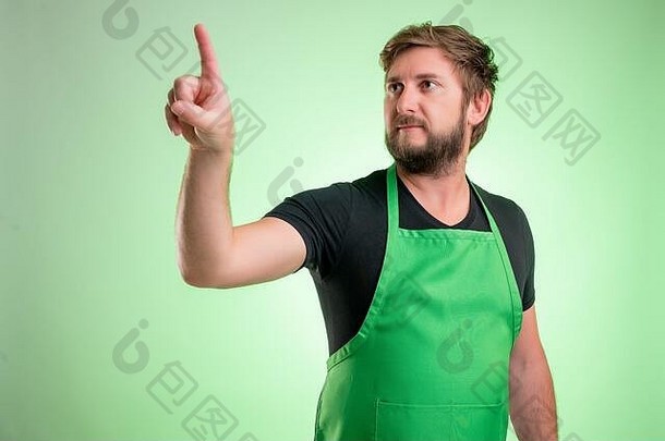 穿着绿色围裙和黑色t恤衫的超市员工，按下绿色背景上隔离的虚拟按钮